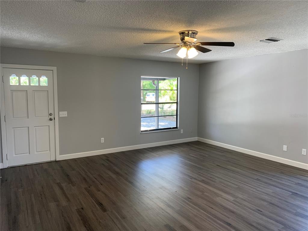 A living room features gray walls, dark wood-look flooring, a ceiling fan, and a front door — 527 HILL STREET UNIT A, EUSTIS, FL
