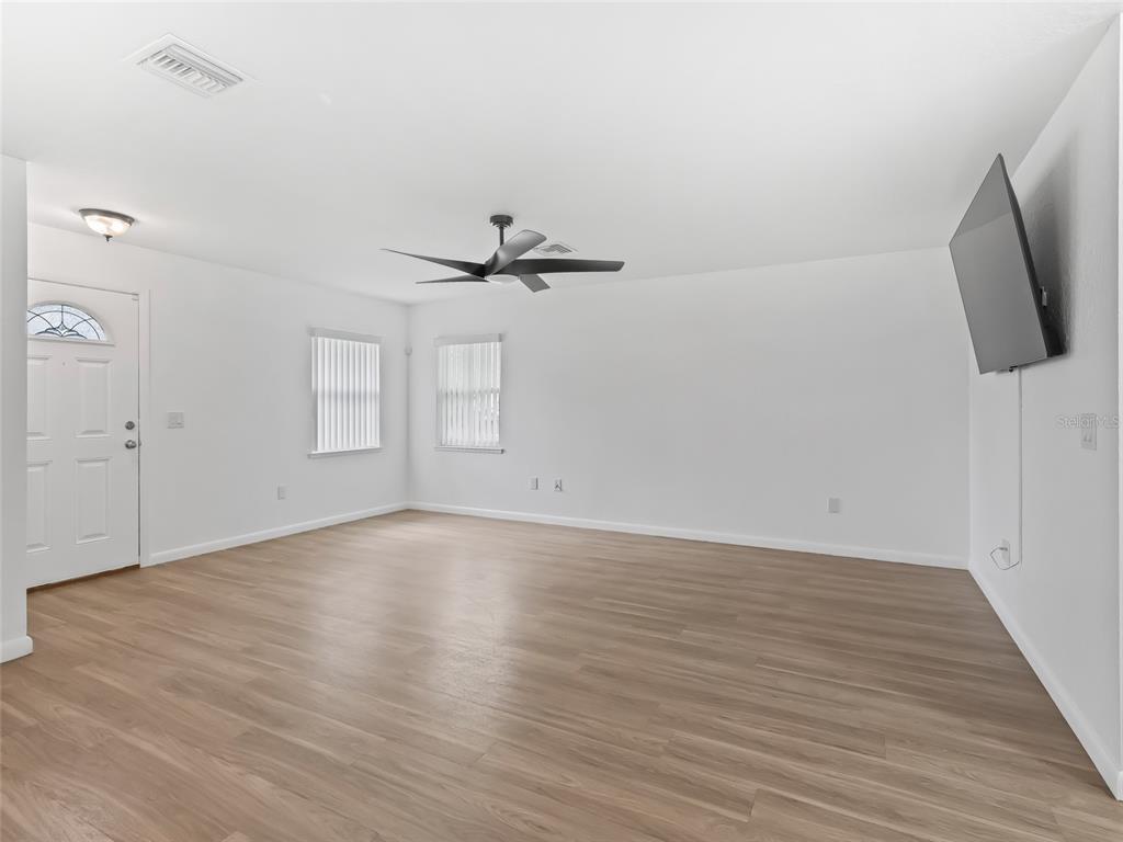 A bright living room features light wood-look flooring, white walls, a ceiling fan, and television — 9318 CR 649, BUSHNELL, FL