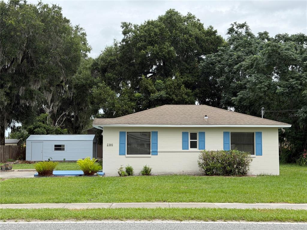 A single-story house with light-colored siding, blue shutters, and a detached shed in the yard — 2301 E WARM SPRINGS AVENUE, COLEMAN, FL