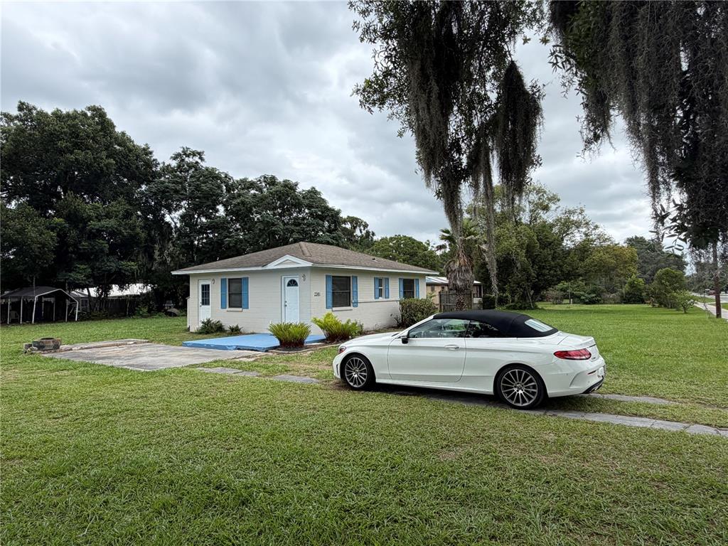 A white single-story house with blue shutters sits on a grassy lot with a car — 2301 E WARM SPRINGS AVENUE, COLEMAN, FL