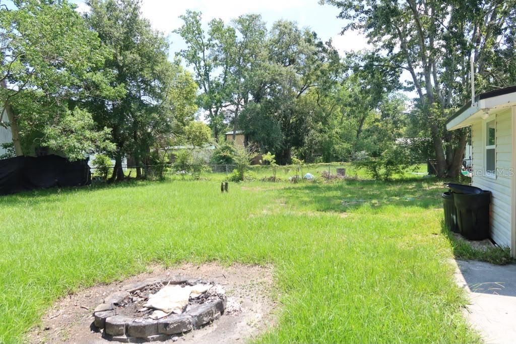 A grassy backyard features a stone fire pit and a chain-link fence near trees — 6731 MOPSY LN, JACKSONVILLE, FL