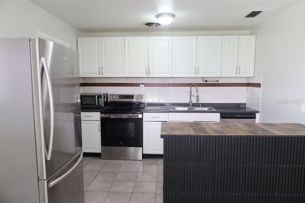 A kitchen features white cabinets, stainless steel appliances, a tiled backsplash, and a dark island — 6731 MOPSY LN, JACKSONVILLE, FL
