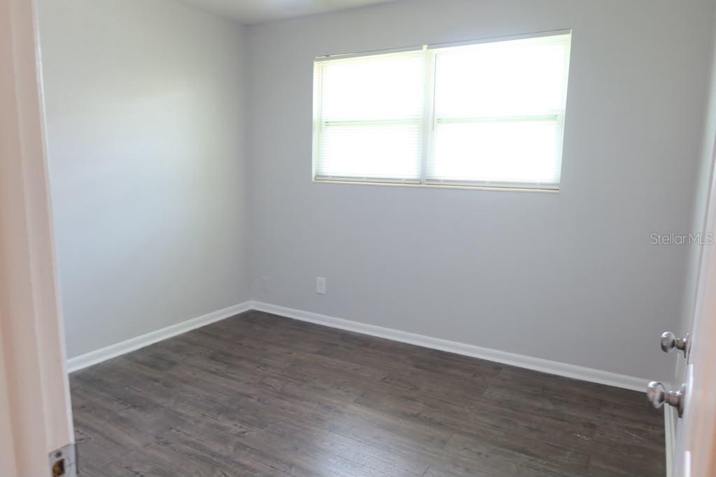An empty bedroom features light gray walls, dark wood-look flooring, and a window with blinds — 6731 MOPSY LN, JACKSONVILLE, FL