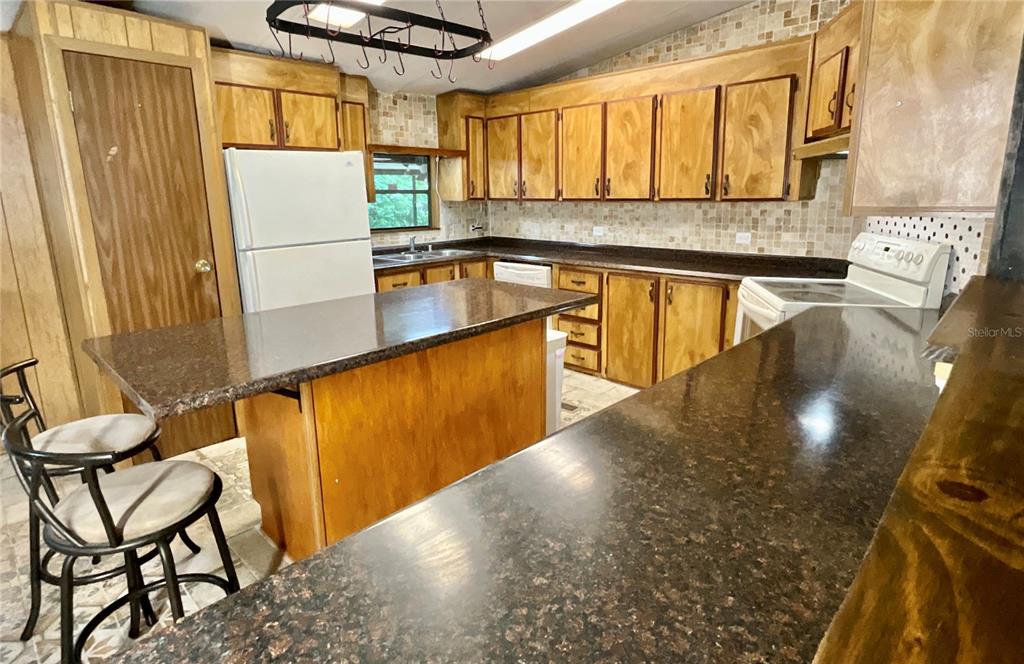 A kitchen features wood cabinets, dark granite countertops, a central island, and a white refrigerator — 13951 NE 140TH STREET, WALDO, FL