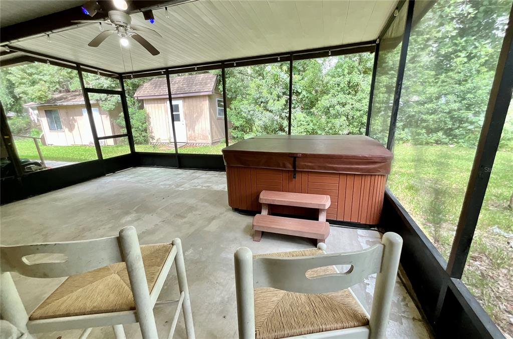 A screened-in porch features a hot tub with steps and two chairs on concrete flooring — 13951 NE 140TH STREET, WALDO, FL