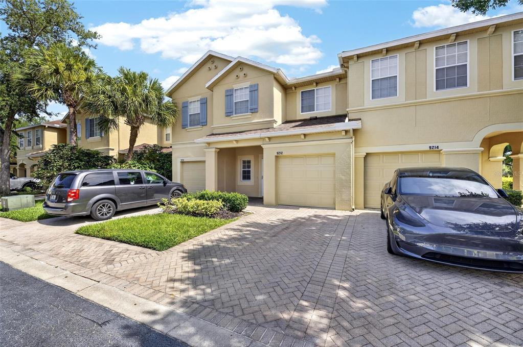 A two-story townhouse exterior with a paved driveway, two garage doors, and parked vehicles — 9212 RIVER ROCK LANE, RIVERVIEW, FL