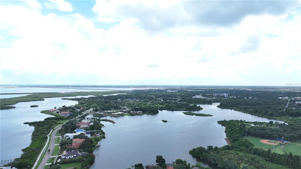 An aerial view shows a coastal neighborhood with houses, a lake, and a baseball field — 560 7TH STREET S, SAFETY HARBOR, FL