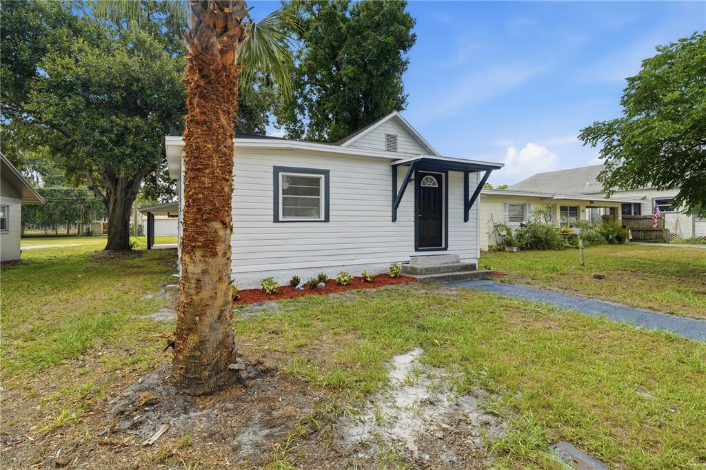 A white, single-story house with a dark front door and a palm tree in front — 515 NEW YORK AVENUE, ST CLOUD, FL