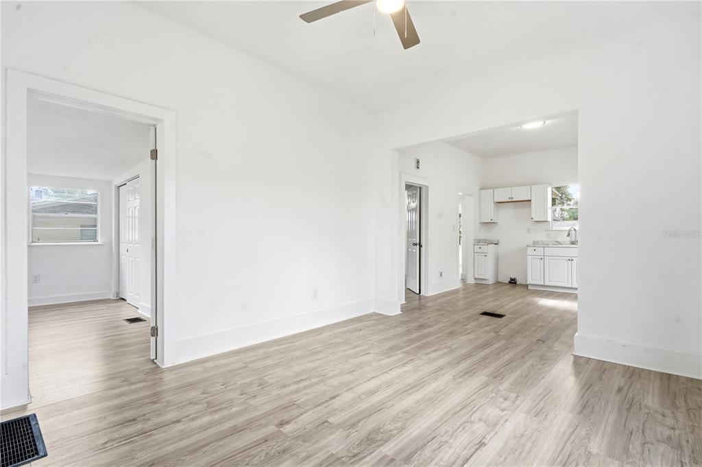 A bright living area with light wood-look flooring leads into a white kitchen — 515 NEW YORK AVENUE, ST CLOUD, FL