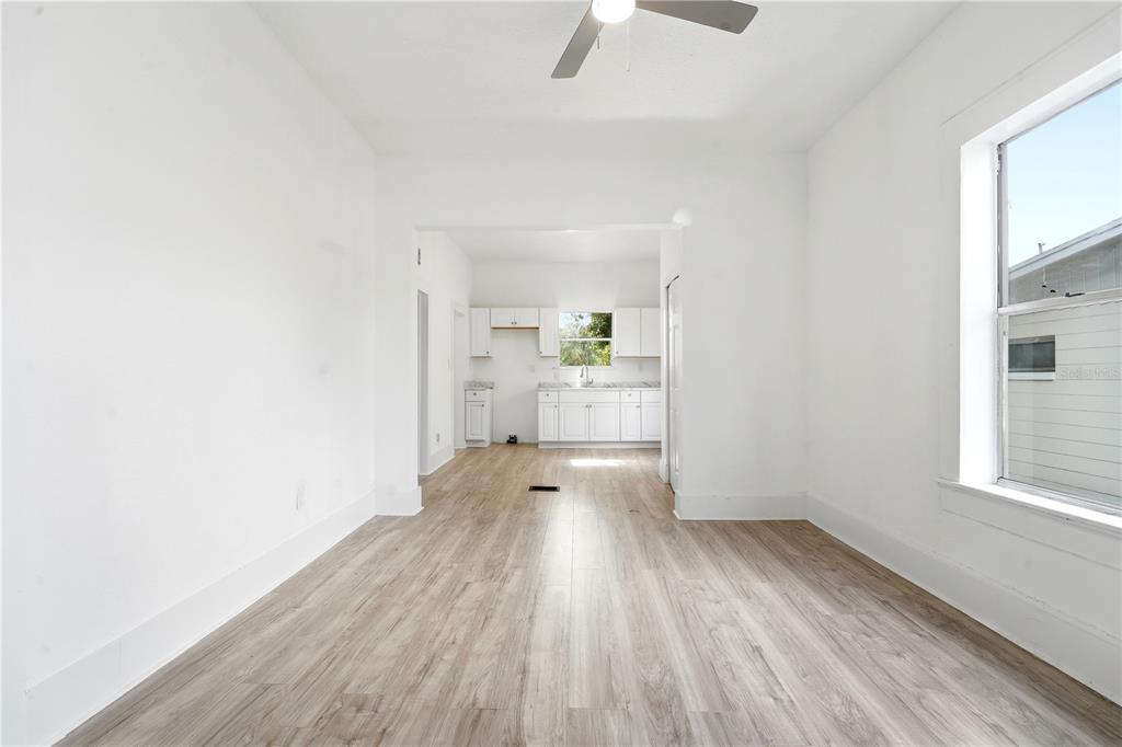 A bright, empty room with light wood-look flooring leads to a kitchen with white cabinets — 515 NEW YORK AVENUE, ST CLOUD, FL