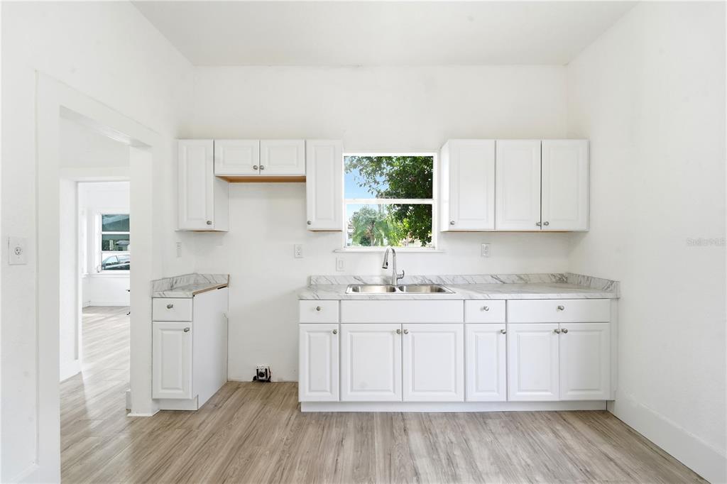 A kitchen features white cabinets, marble-look countertops, a stainless steel sink, and wood-look flooring — 515 NEW YORK AVENUE, ST CLOUD, FL