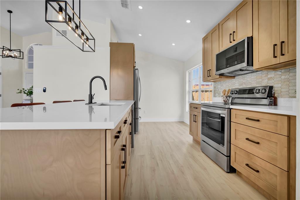 A modern kitchen features light wood cabinets, white countertops, stainless steel appliances, and pendant lighting — 8320 SOUTHERN FOREST DRIVE, ORLANDO, FL