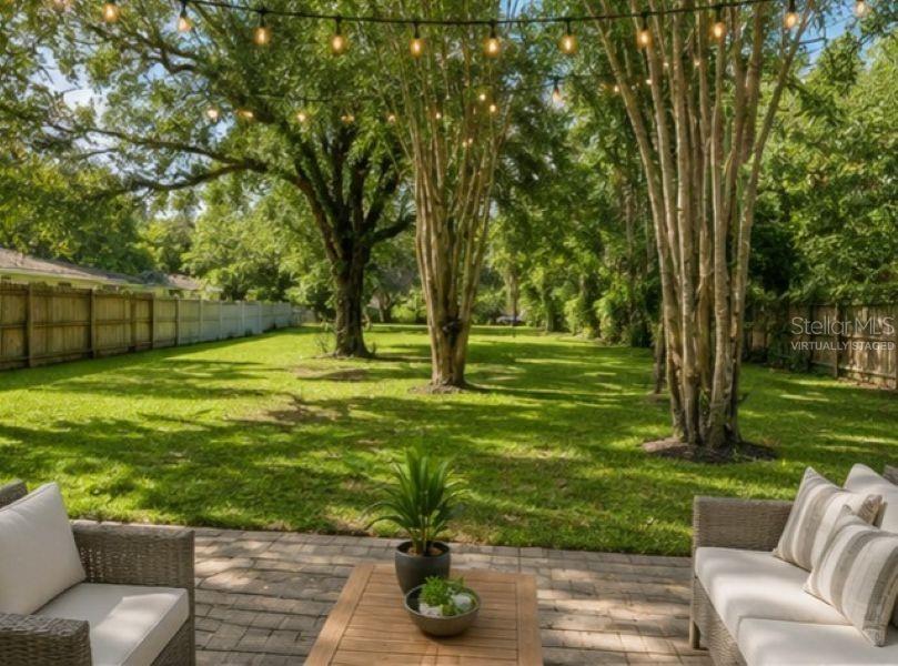 A patio with outdoor furniture overlooks a large, tree-filled backyard with string lights — 1714 2ND AVENUE E, BRADENTON, FL