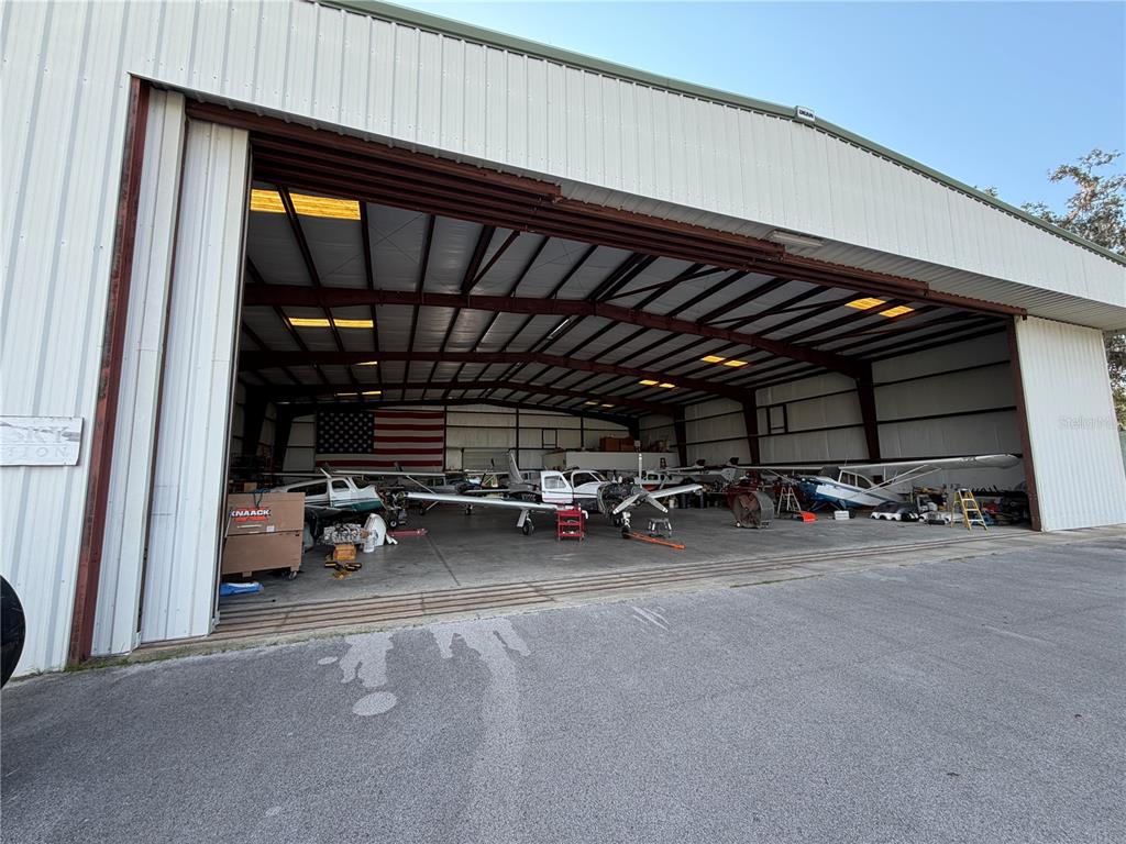 A large open-air aircraft hangar houses several small airplanes and a large American flag — 10601 SW 147TH CIRCLE, DUNNELLON, FL