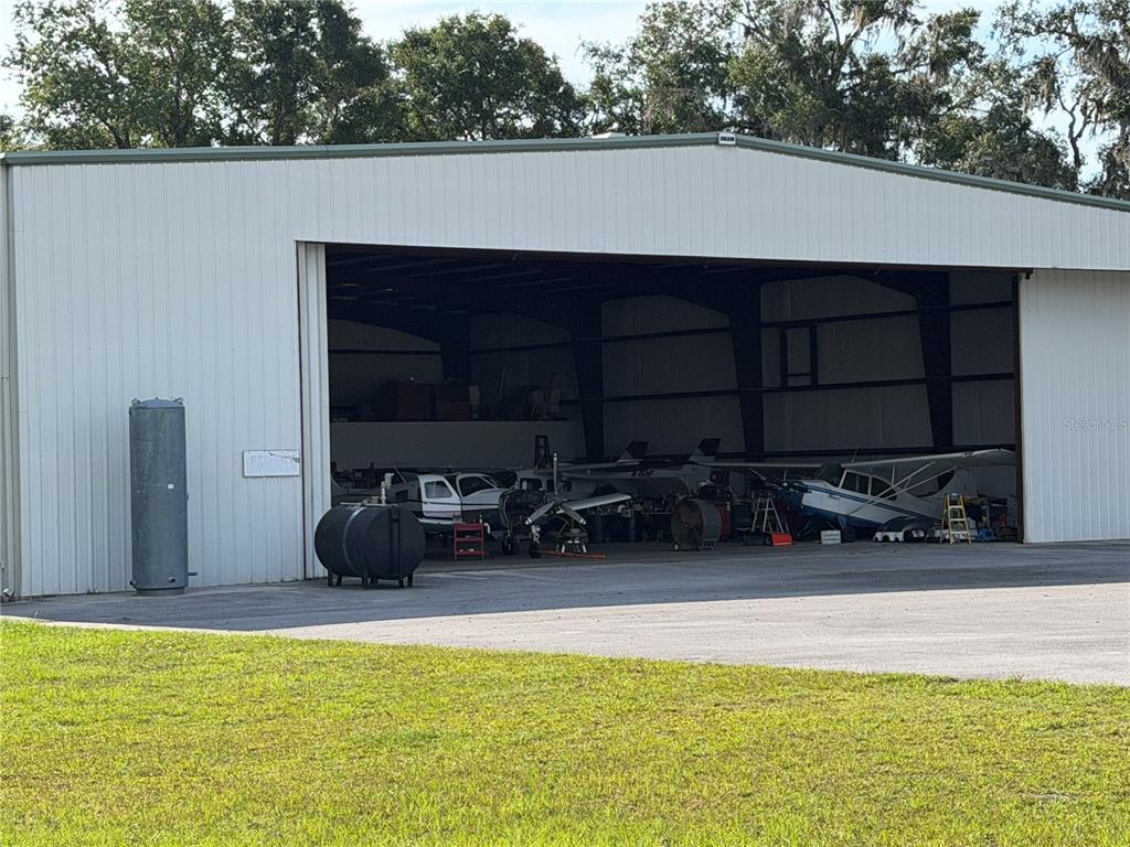 An open airplane hangar contains several small aircraft and equipment on a concrete apron — 10601 SW 147TH CIRCLE, DUNNELLON, FL