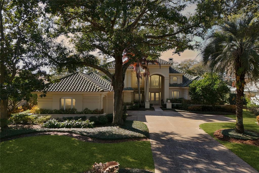 A two-story stucco house with a tile roof, large oak tree, and concrete driveway — 5145 LATROBE DRIVE, WINDERMERE, FL