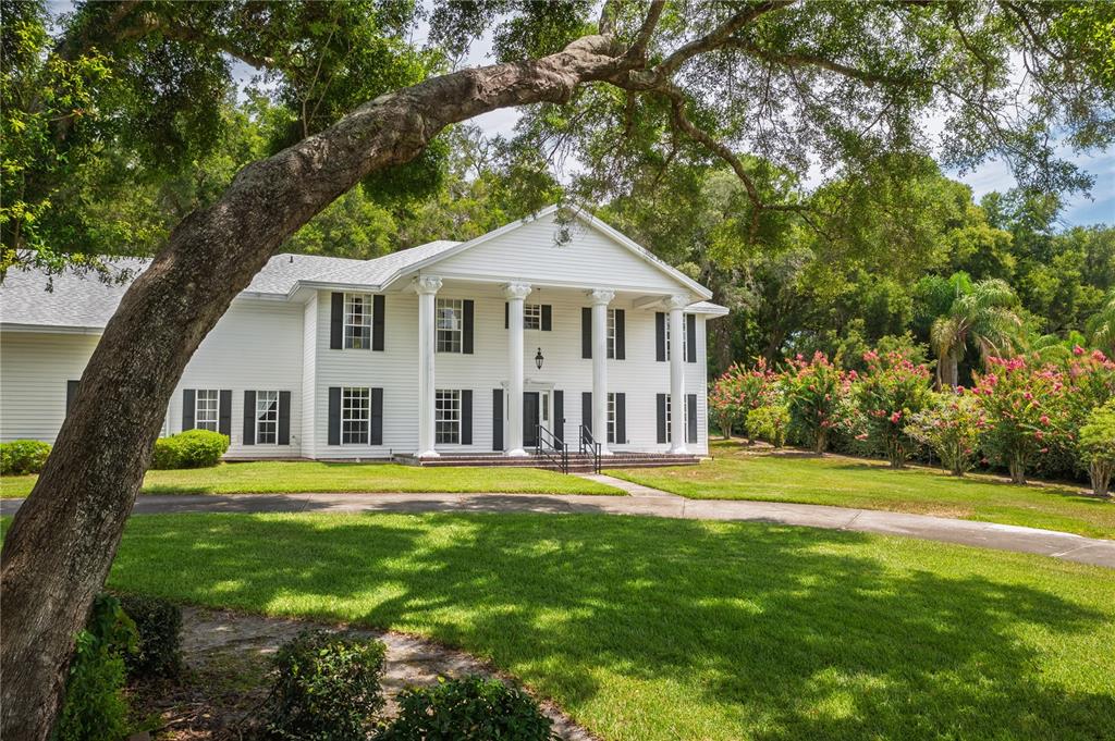 A two-story white house with a columned front porch sits on a grassy lawn — 7219 CHESTERHILL CIRCLE, MOUNT DORA, FL