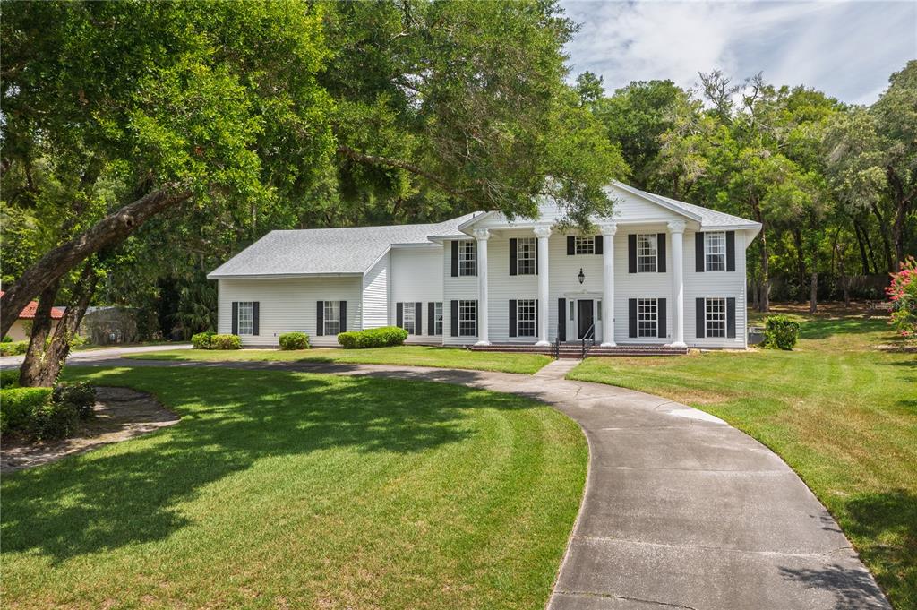 A two-story white colonial-style house features a columned portico and a curved concrete driveway — 7219 CHESTERHILL CIRCLE, MOUNT DORA, FL