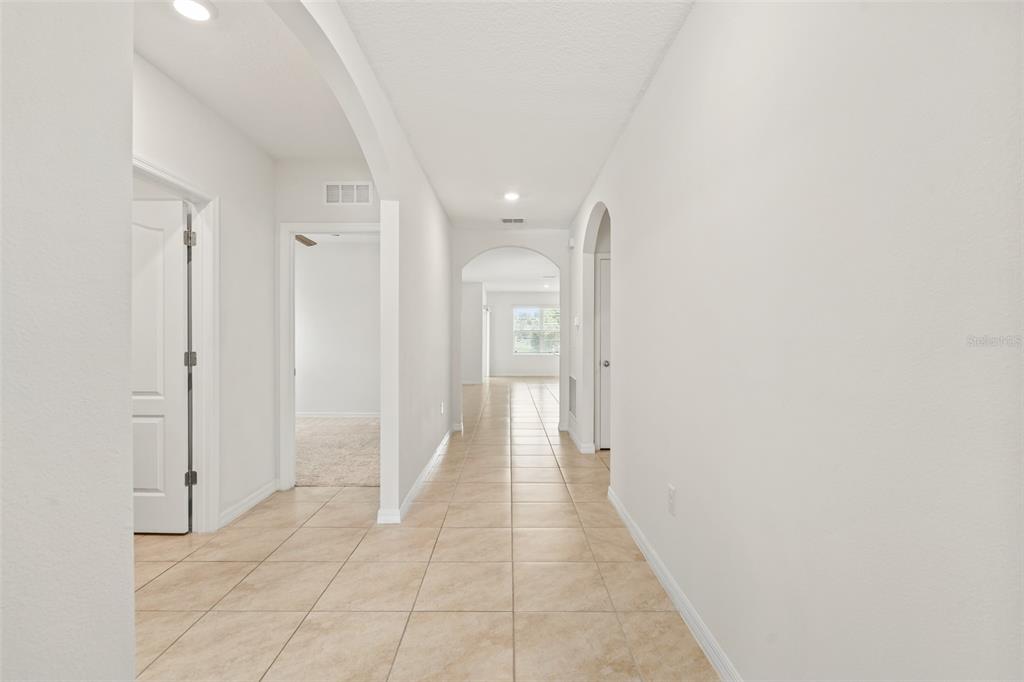 A long hallway with light-colored tile flooring leads to a room with a window — 5274 MAYOR DRIVE, ST CLOUD, FL