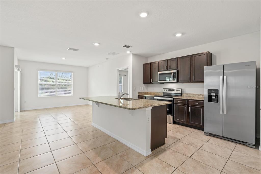 A kitchen with dark wood cabinets, granite countertops, and stainless steel appliances opens to a room — 5274 MAYOR DRIVE, ST CLOUD, FL
