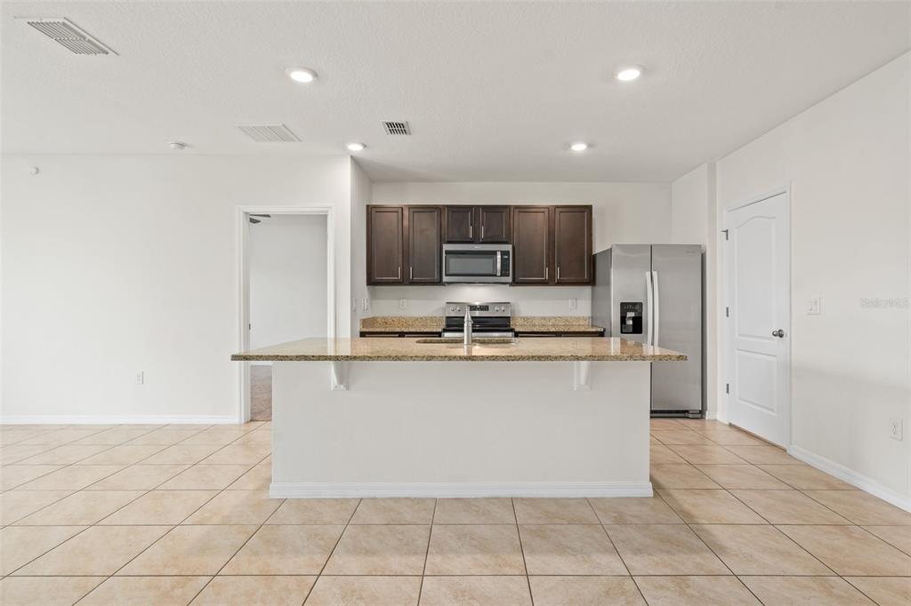 A kitchen features dark wood cabinets, granite countertops, stainless steel appliances, and a central island — 5274 MAYOR DRIVE, ST CLOUD, FL