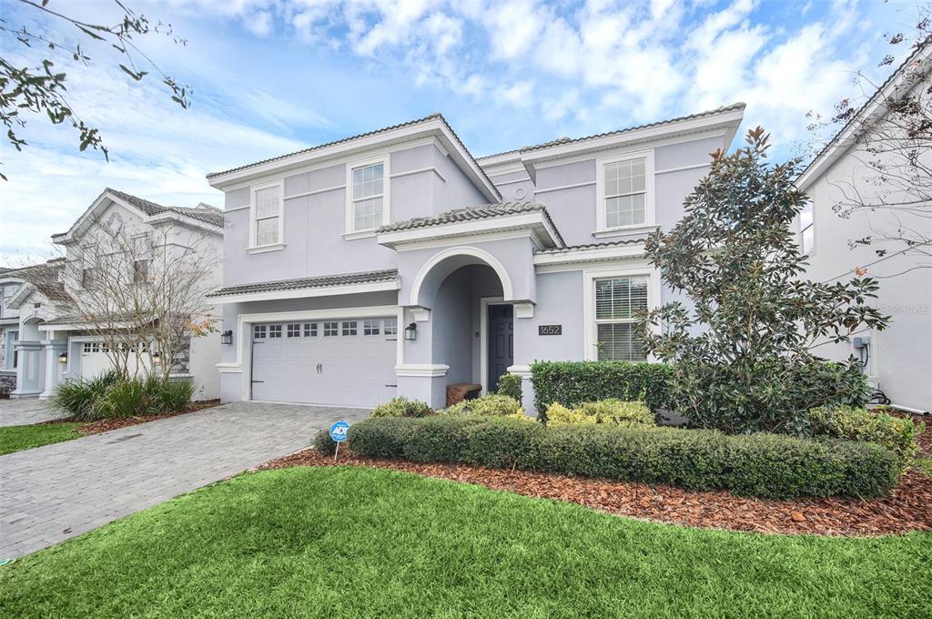 A two-story light blue house with a paved driveway, arched entryway, and manicured landscaping — 1652 MOON VALLEY DRIVE, DAVENPORT, FL