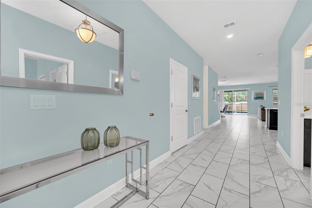 A hallway with light blue walls, white trim, and white marble-look tile flooring leads forward — 1652 MOON VALLEY DRIVE, DAVENPORT, FL