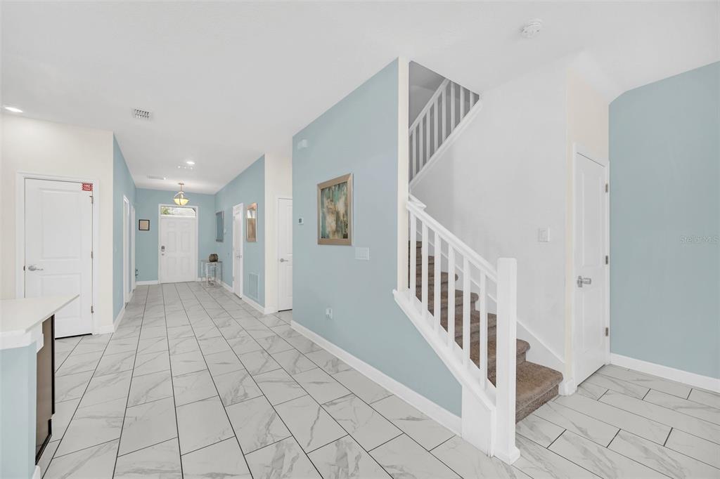 An entryway features light blue walls, white trim, a staircase, and white marble-look tile flooring — 1652 MOON VALLEY DRIVE, DAVENPORT, FL