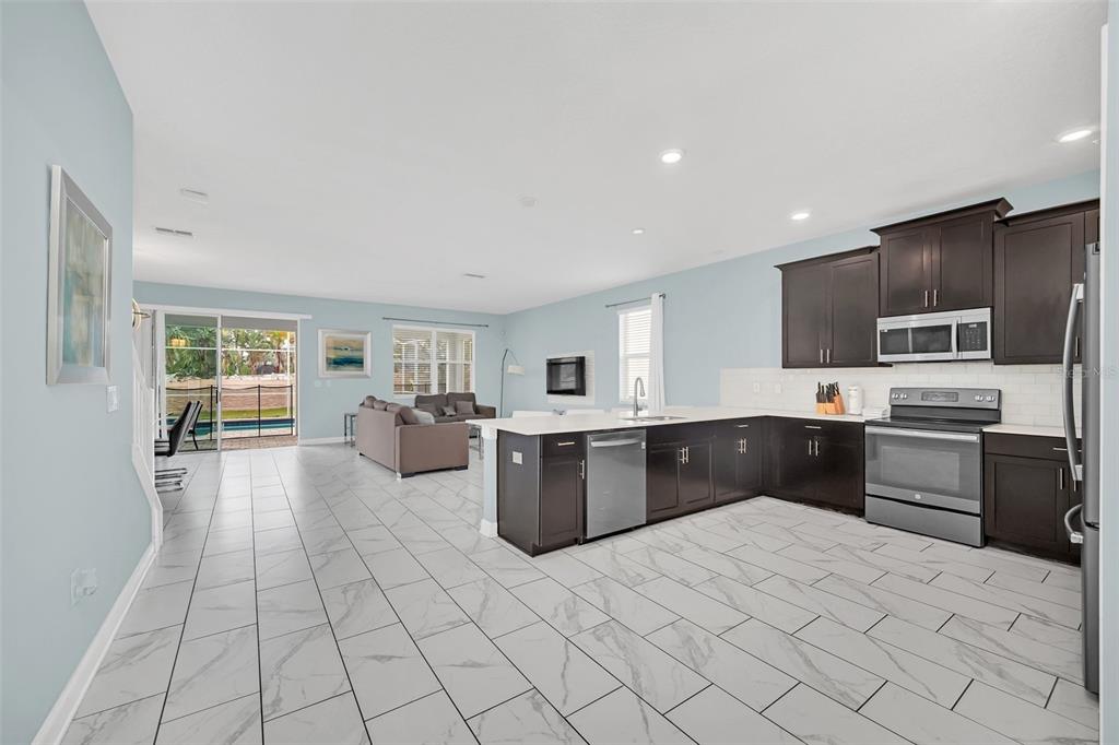 An open-concept kitchen and living area featuring dark cabinetry, white countertops, and light tile flooring — 1652 MOON VALLEY DRIVE, DAVENPORT, FL