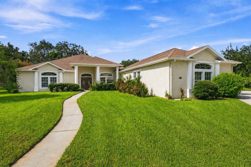 A single-story house with a beige stucco exterior, a brown roof, and a concrete walkway — 13750 DOWLING LANE, ODESSA, FL