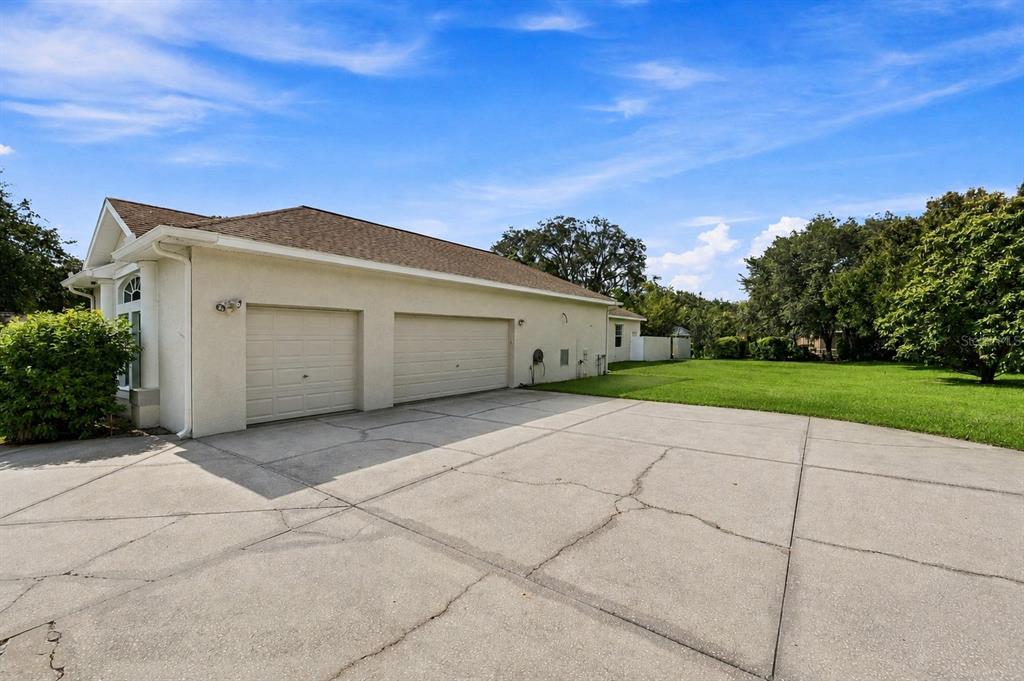 A beige house with a three-car garage and a large concrete driveway under a blue sky — 13750 DOWLING LANE, ODESSA, FL
