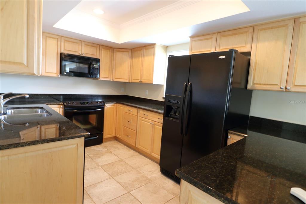 A kitchen features light wood cabinets, black granite countertops, and black appliances — 2465 HERON TERRACE UNIT 202B, CLEARWATER, FL