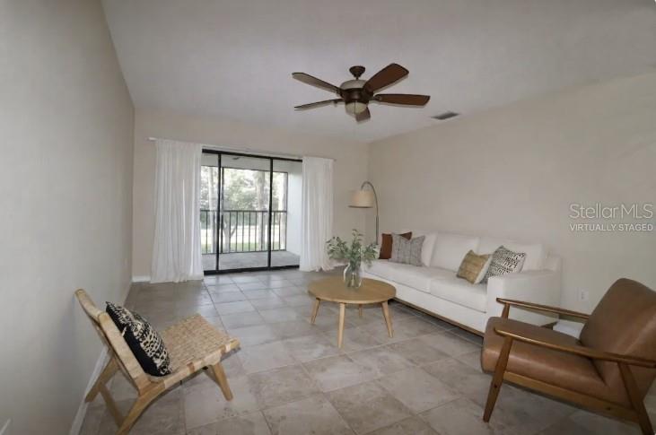 This living room features tile flooring, a ceiling fan, and sliding glass doors to a balcony — 2465 HERON TERRACE UNIT 202B, CLEARWATER, FL