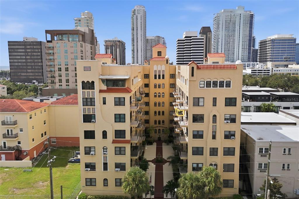 An exterior view of a multi-story, tan-colored apartment building with a central courtyard and balconies — 130 4TH AVENUE N UNIT 504, ST PETERSBURG, FL