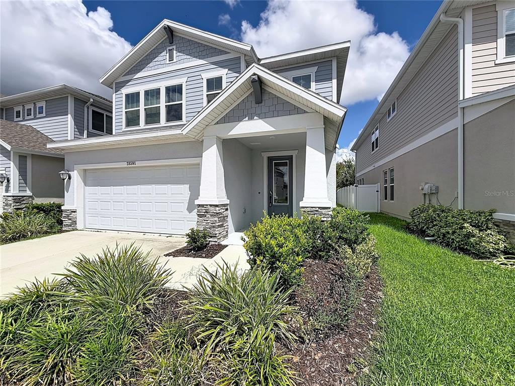 A two-story suburban house with light blue siding, a white garage, and a covered entryway — 28591 COZY CREEK DRIVE, WESLEY CHAPEL, FL