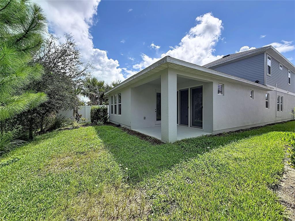 A view of a house exterior featuring a covered patio and a grassy backyard — 28591 COZY CREEK DRIVE, WESLEY CHAPEL, FL