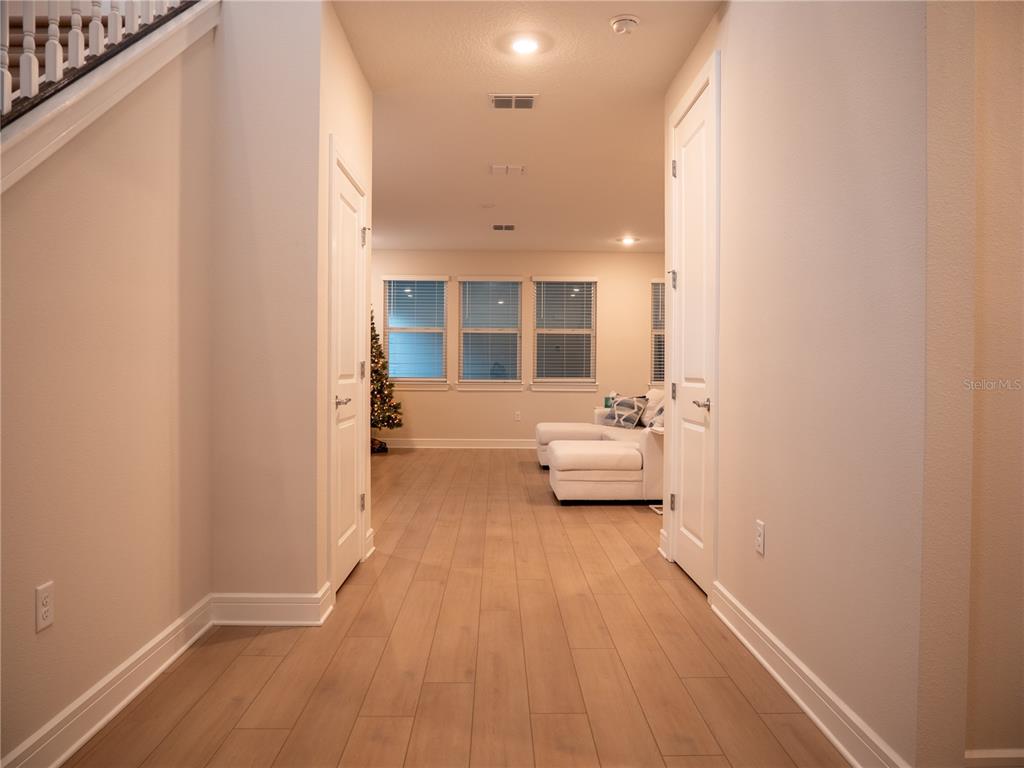 A hallway with light wood flooring leads to a living area with white furniture — 6518 WINDING PATH WAY, ST CLOUD, FL