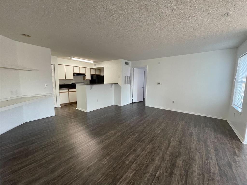 An open-concept living area features dark wood-look flooring, white walls, and a kitchen with cabinets — 2202 KEY WEST COURT UNIT 616, KISSIMMEE, FL