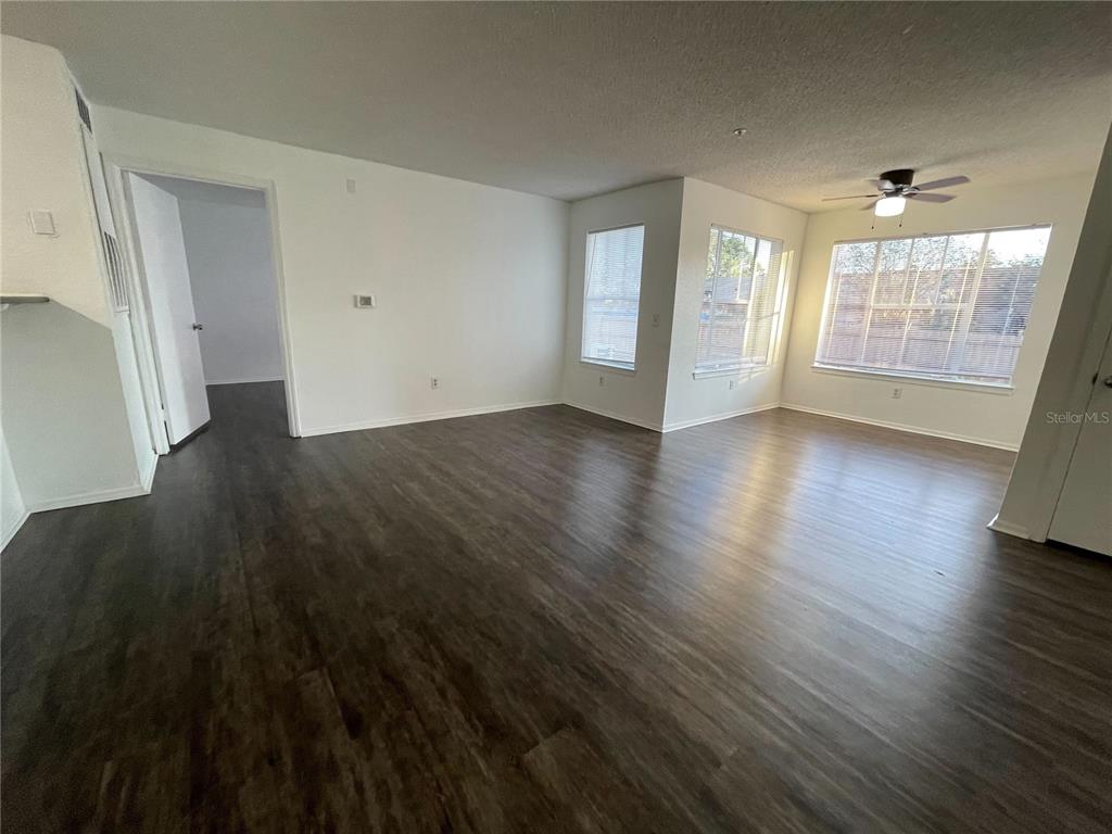 An empty living room features dark wood-look flooring, white walls, and three windows — 2202 KEY WEST COURT UNIT 616, KISSIMMEE, FL