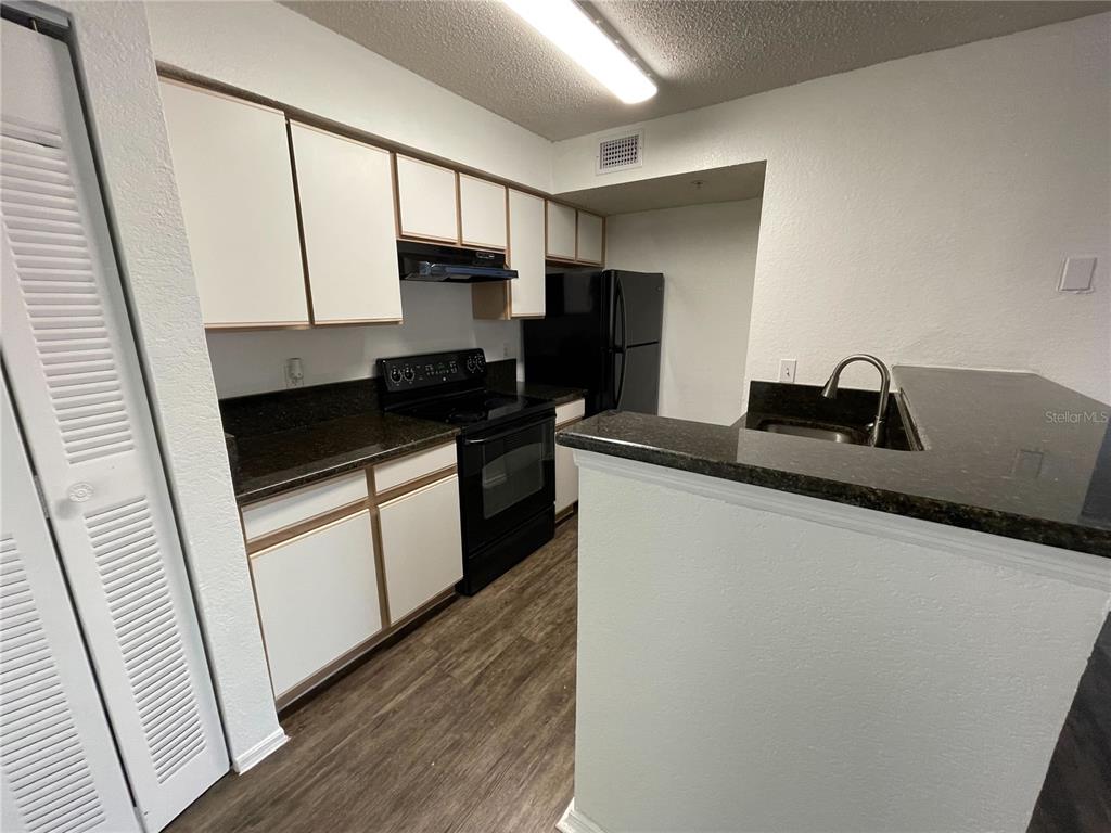 A kitchen features white cabinets, dark countertops, black appliances, and wood-look flooring — 2202 KEY WEST COURT UNIT 616, KISSIMMEE, FL