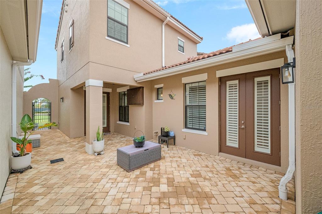 A paved courtyard patio features a small table, potted plants, and double glass doors — 8870 NAPOLO DRIVE, MELBOURNE, FL