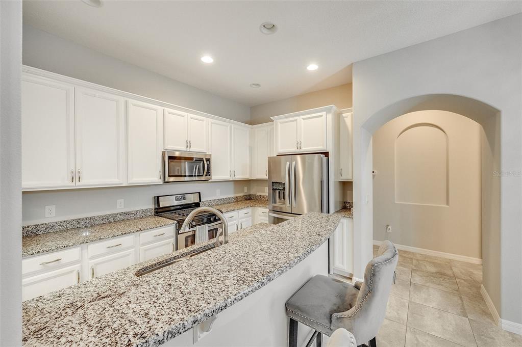 A kitchen with white cabinets, granite countertops, stainless steel appliances, and a breakfast bar — 8870 NAPOLO DRIVE, MELBOURNE, FL