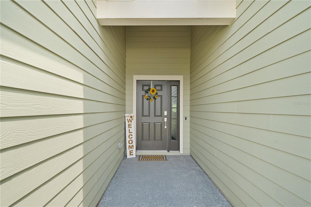 A covered entryway features light green horizontal siding, a gray front door, and a welcome sign — 13669 NW CONVERGENCE BOULEVARD, ALACHUA, FL