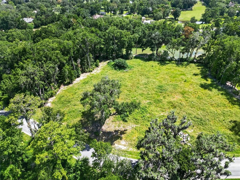 An aerial view shows a vacant, grassy lot surrounded by dense trees and a road — TBD SE 12 CIRCLE, OCALA, FL