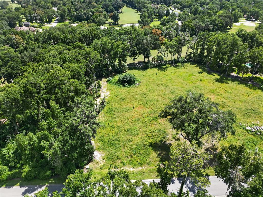An aerial view shows a vacant, grassy lot bordered by dense trees and a road — TBD SE 12 CIRCLE, OCALA, FL