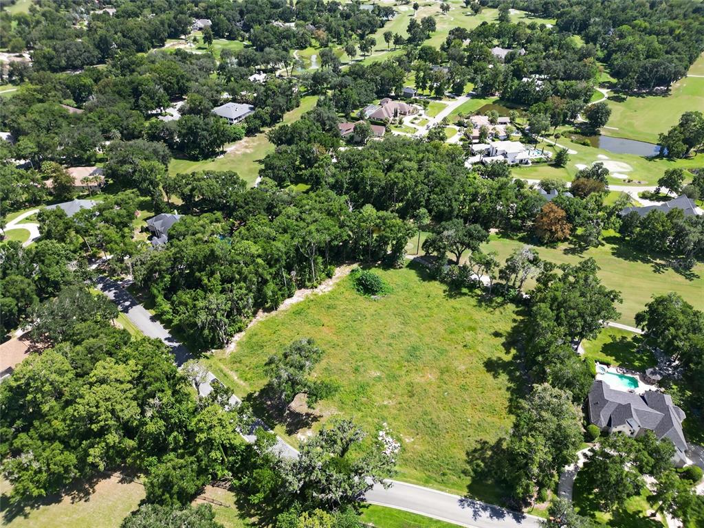 An aerial view shows a vacant, grassy residential lot surrounded by trees and nearby houses — TBD SE 12 CIRCLE, OCALA, FL
