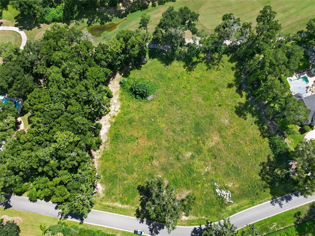 An aerial view shows a vacant, grassy residential lot bordered by trees and a curved road — TBD SE 12 CIRCLE, OCALA, FL