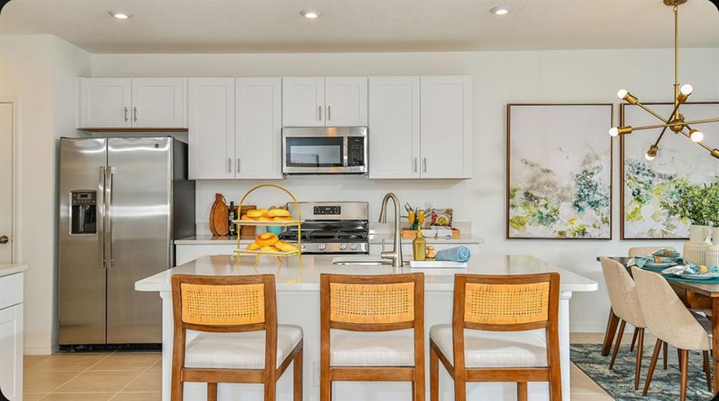 A modern kitchen features white cabinets, a large quartz island, and stainless steel appliances — 13844 SHELLMORE AVENUE, PALMETTO, FL