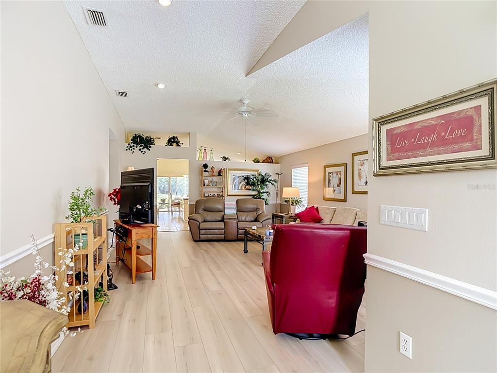 A living room features light wood-look flooring, a vaulted ceiling, and a red recliner chair — 7828 CRAIGHURST LOOP, NEW PORT RICHEY, FL
