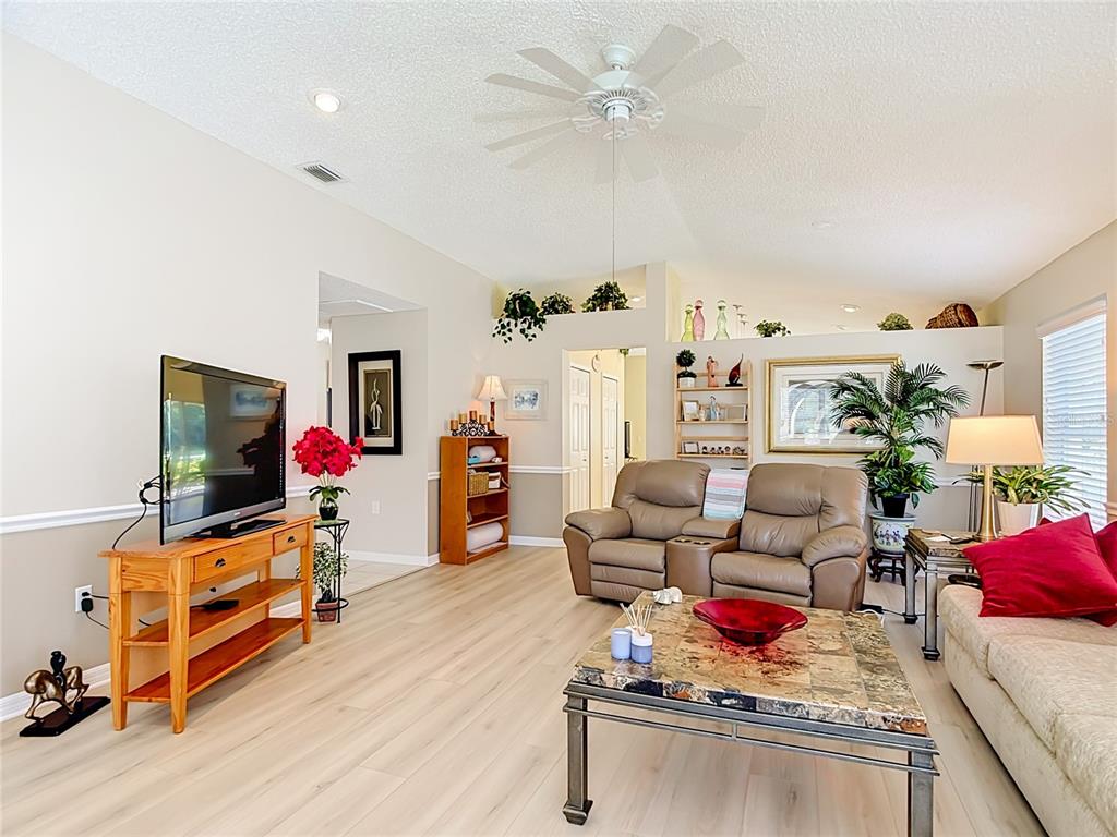 A living room features light wood-look flooring, a ceiling fan, and a tan leather loveseat — 7828 CRAIGHURST LOOP, NEW PORT RICHEY, FL